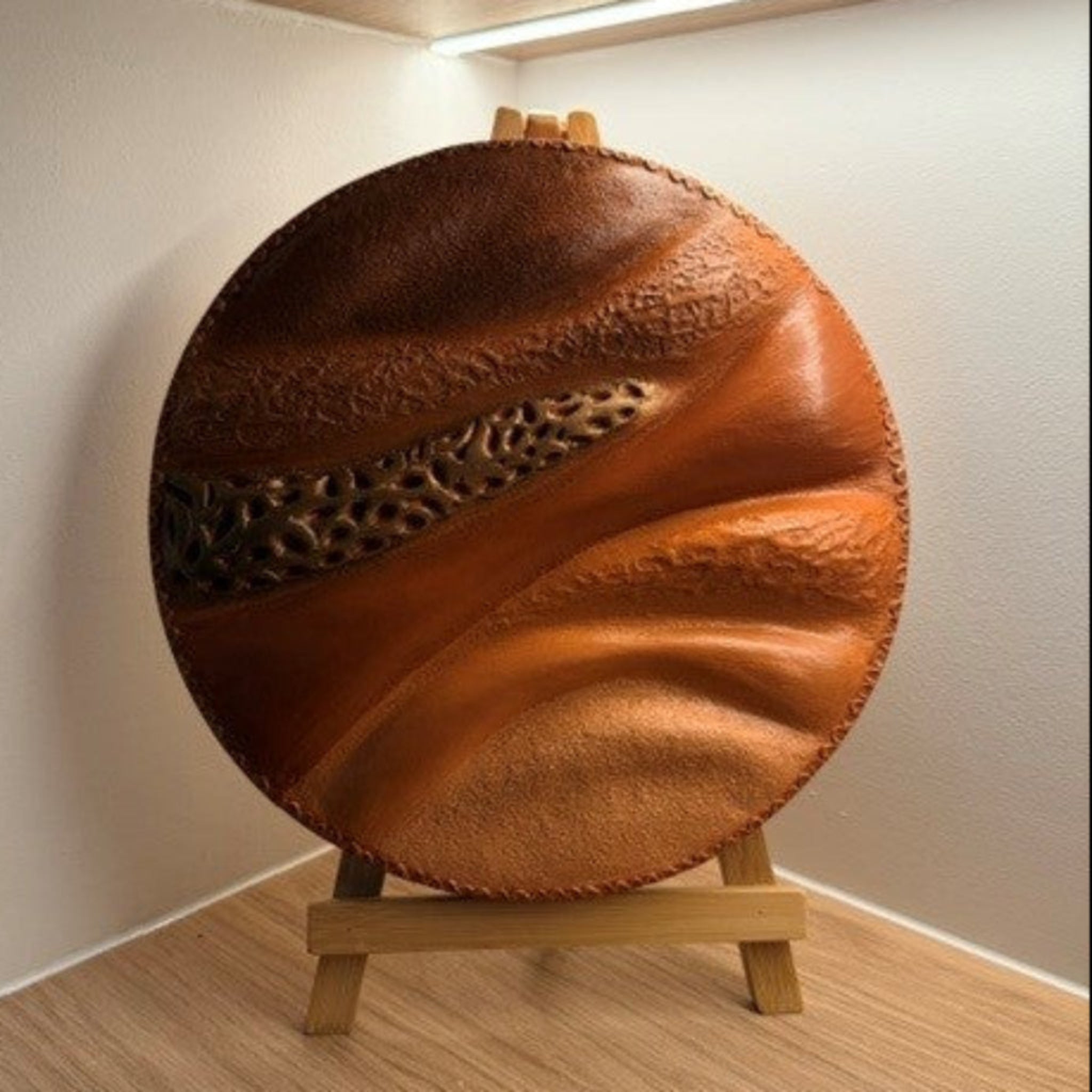 Round textured sculpture painting  in earthy colours on shelf under artificial strip light