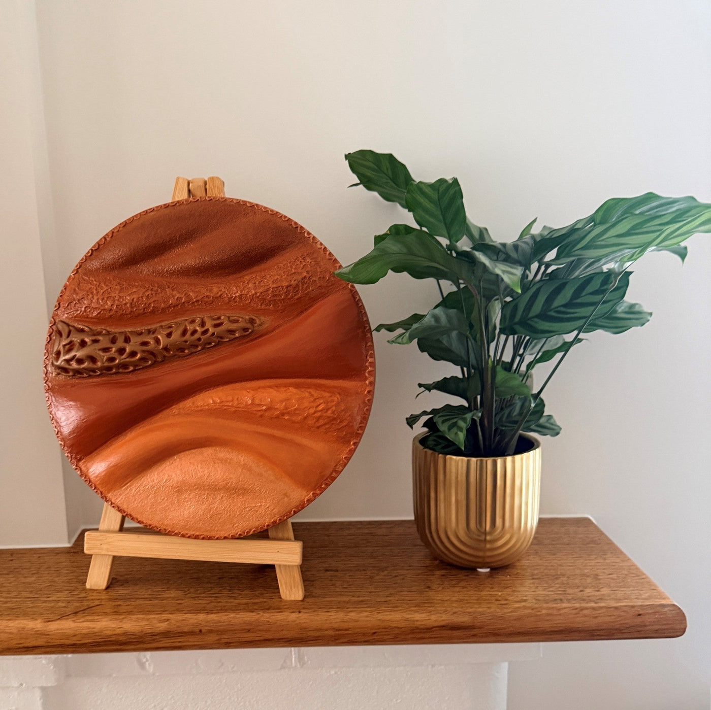 Round textured sculpture painting in earthy tone styled with plant in gold pot in natural light
